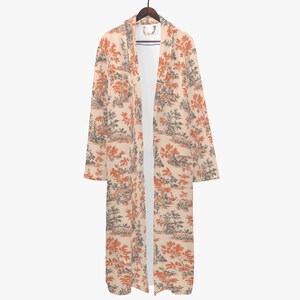 May include: A long, open-front robe with a cream-colored background and a repeating pattern of orange and gray trees and landscapes. The robe is hanging on a wooden hanger, showcasing its full length and design.