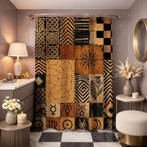 Op de afbeelding: Een patchwork douchegordijn met diverse geometrische en hemelse ontwerpen in zwart, goud en bruin. Het gordijn heeft een kompasroos, sterrenbeelden en andere symbolen. Het gordijn hangt in een badkamer met een goudkleurige spiegel.