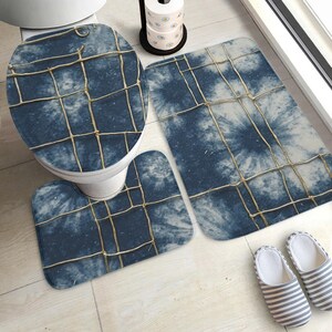 Könnte beinhalten: Ein dreiteiliges Badezimmer-Set mit blauem Batikmuster und einem Gitterdesign. Das Set umfasst einen Toilettensitzbezug, eine Konturmatte und eine rechteckige Badematte. Das Set ist so konzipiert, dass es das Badezimmerdekor koordiniert und aufwertet.