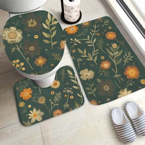 May include: A bathroom set comprising a toilet seat cover, a U-shaped mat, and a rectangular rug. The set displays a dark green floral pattern in orange, yellow, and brown. A pair of striped slippers is visible on the floor. The set is designed for a bathroom.