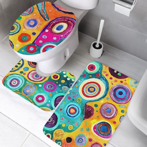 Könnte beinhalten: Ein Badezimmer-Teppichset mit einem farbenfrohen abstrakten Design mit Kreisen in Blautönen, Grün, Gelb, Rot und Rosa. Das Set beinhaltet einen Toilettensitzbezug, einen kleinen Teppich für die Toilettenbasis und einen größeren Teppich für den Boden.