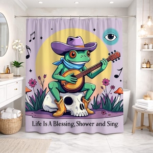 May include: A whimsical shower curtain featuring a cartoon frog playing a banjo while wearing a cowboy hat and boots. The frog is sitting on a skull, with musical notes and the text "Life Is A Blessing, Shower and Sing."