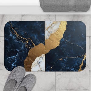 Könnte beinhalten: Eine rechteckige Badematte mit einem Design aus marineblauem und goldenem Marmor. Die Matte hat ein goldenes Adernmuster und einen weißen Marmorabschnitt. Graue Hausschuhe befinden sich am unteren Rand der Matte.