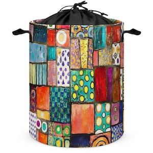 Könnte beinhalten: Ein zylindrischer Wäschekorb mit einem farbenfrohen Patchwork-Design. Das Muster zeigt eine Vielzahl rechteckiger Formen in Rot-, Orange-, Blau- und Gelbtönen. Er hat einen schwarzen Kordelzugverschluss und schwarze Griffe.