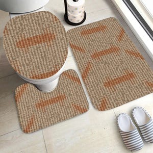 May include: A bathroom set featuring a toilet seat cover, a contour rug, and a rectangular rug. The set has a beige and brown textured pattern with orange stripes. Two striped slippers are on the floor.