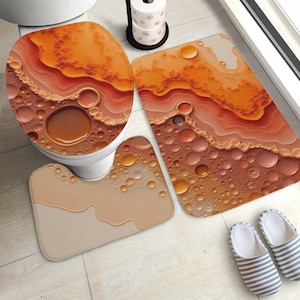 May include: A bathroom set featuring a toilet seat cover, a rectangular bath mat, and a U-shaped contour rug. Each piece displays an abstract design of orange and beige liquid bubbles and flowing layers, creating a cohesive, textured visual pattern.
