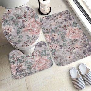 Könnte beinhalten: Ein dreiteiliges Badezimmer-Teppichset mit einem floralen Muster in Rosa-, Grau- und Grüntönen. Das Set beinhaltet einen Toilettensitzbezug, einen Kontur-Teppich und eine größere Badematte.