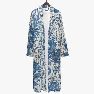 Op de afbeelding: Lange, openvallende kimono met een blauw en wit bloemenpatroon, hangend aan een houten hanger. De kimono heeft een gedetailleerd ontwerp met botanische en abstracte elementen en heeft twee voorzakken.