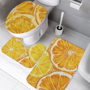 May include: A three-piece bathroom set comprising a toilet lid cover, a U-shaped contour rug, and a rectangular bath mat. Each item features a vibrant, repeating pattern of sliced oranges in shades of bright yellow and deep orange.