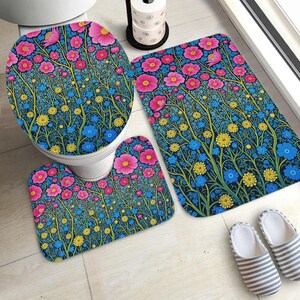May include: A bathroom set featuring a toilet seat cover, a rectangular bath mat, and a U-shaped contour rug, all decorated with a vibrant floral pattern of pink, yellow, and blue flowers on a dark blue background with thin green stems.