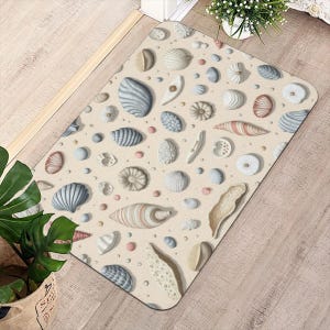 Könnte beinhalten: Rechteckige, beige Fußmatte mit einem Muster aus verschiedenen Muscheln in Blau-, Beige- und Rosatönen. Die Muscheln sind über die Matte verstreut und erzeugen ein Strand-Thema. Die Matte ist wahrscheinlich aus einem strapazierfähigen Material.