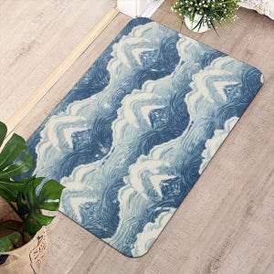 Puede incluir: Una alfombra rectangular con un diseño de olas en azul y blanco. La alfombra está colocada sobre un suelo de madera clara. En el fondo se ven una planta en maceta y una pequeña planta decorativa. El diseño de la alfombra evoca el agua.