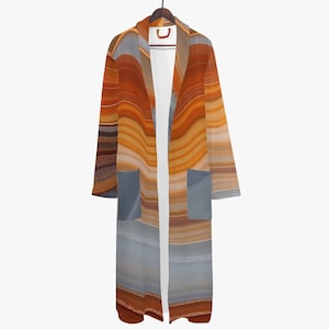 May include: A long, open-front robe with a flowing design. The robe features a pattern of horizontal stripes in shades of orange, brown, and gray. It has two front pockets and is hanging on a wooden hanger.