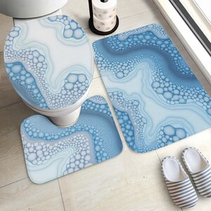 Può includere: Un set da bagno composto da un copriwater, un tappetino da bagno rettangolare e un tappeto a U per il contorno del WC, tutti decorati con un motivo astratto blu e bianco di forme fluide e cerchi simili a bolle.