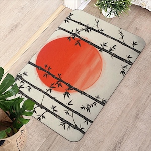 May include: A rectangular floor mat featuring a cream-colored background with a large, solid red circle in the center. The design includes several black bamboo stalks crossing diagonally across the mat, adorned with small, pointed leaves.
