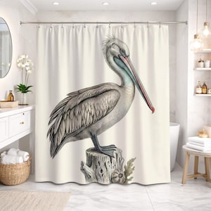 May include: A shower curtain featuring a detailed illustration of a pelican perched on a tree stump. The bird has gray and white feathers, a long red and blue beak, and is set against a cream-colored background. The artwork has a vintage, botanical illustration style.