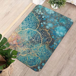 Op de afbeelding: Rechthoekige vloermat met een abstract ontwerp in tinten van turquoise, blauw en goud. Het patroon lijkt op een netwerk van aderen of cellen, met een aquareleffect. De mat ligt op een lichte houten vloer.