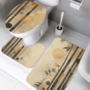 May include: A three-piece bathroom set featuring a bamboo design. The set includes a toilet seat cover, a U-shaped rug, and a rectangular rug. The design features bamboo stalks, orange circles, and a beige background.