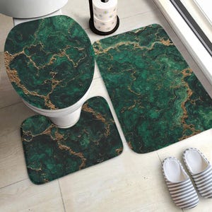 Può includere: Un set da bagno con un design a marmo verde e oro. Il set comprende un copriwater, un tappeto sagomato e un tappetino da bagno rettangolare. Il design è verde scuro con venature dorate. È visibile un paio di pantofole a righe.