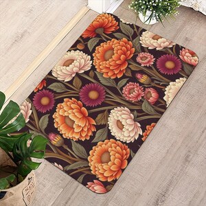Può includere: Un tappetino rettangolare caratterizzato da un denso motivo botanico di grandi fiori di crisantemo a strati nei toni dell'arancione, crema e magenta su uno sfondo marrone scuro con foglie e steli verdi in tutto il disegno.