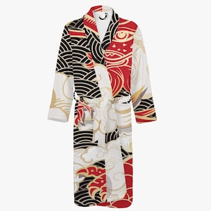 Peut inclure: Une robe de chambre blanche avec un motif d'inspiration japonaise noir, rouge et or. La robe a des manches longues et une ceinture à nouer.