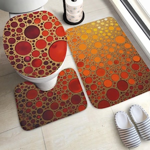 Peut inclure: Un ensemble de salle de bain comprenant une housse de siège de toilette, un tapis de bain rectangulaire et un tapis de contour, tous ornés d'un motif répétitif de cercles dans des tons de rouge, orange et jaune sur fond beige, avec des chaussons rayés.