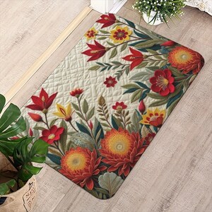 May include: Rectangular floral rug featuring a cream-colored quilted background. The rug is adorned with vibrant red, yellow, and orange flowers, along with green leaves. The design is symmetrical, with flowers along the edges and corners.