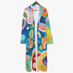 Könnte beinhalten: Langer, offen geschnittener Bademantel mit einem lebendigen abstrakten Aquarelldesign. Der Bademantel weist eine Mischung aus blauen, orangefarbenen, rosa und gelben Formen auf. Er hängt an einem Holzbügel vor weißem Hintergrund.