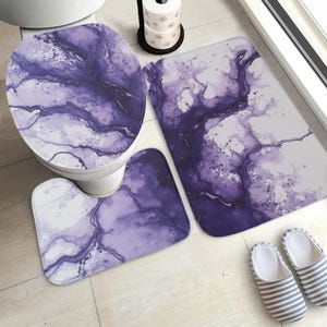 May include: A bathroom set featuring a toilet seat cover, a contour rug, and a rectangular bath mat. The set has a purple and white marbled design. A pair of striped slippers is next to the bath mat.