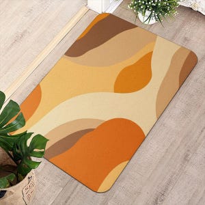Puede incluir: Una alfombrilla rectangular con un patrón abstracto de formas orgánicas fluidas en varios tonos de naranja cálido, amarillo dorado, beige y marrón oscuro. La alfombrilla tiene esquinas redondeadas y una textura de superficie lisa y plana.