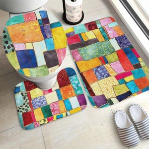 May include: A colorful bathroom set featuring a toilet seat cover, a bath mat, and a contour rug. The set has a patchwork design with various colors including blue, orange, yellow, and green. Striped slippers are next to the bath mat.