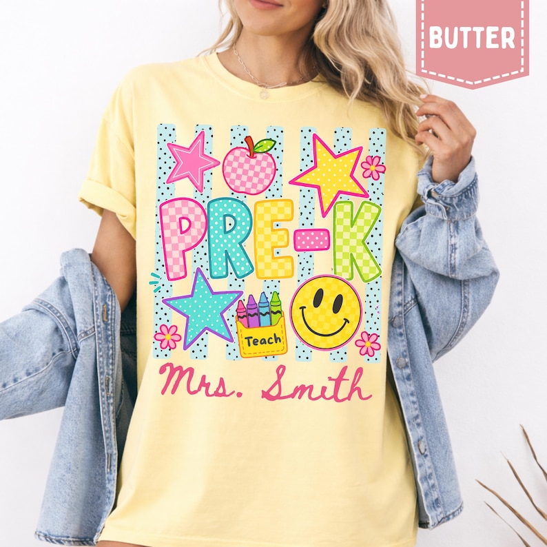 Pode incluir: Uma t-shirt amarelo-manteiga com um gr&aacute;fico que inclui o texto PRE-K e Mrs. Smith. O design apresenta uma ma&ccedil;&atilde; axadrezada, uma estrela amarela, uma rosa, uma turquesa, uma cara sorridente e uma caixa de l&aacute;pis de cor com a palavra Teach.