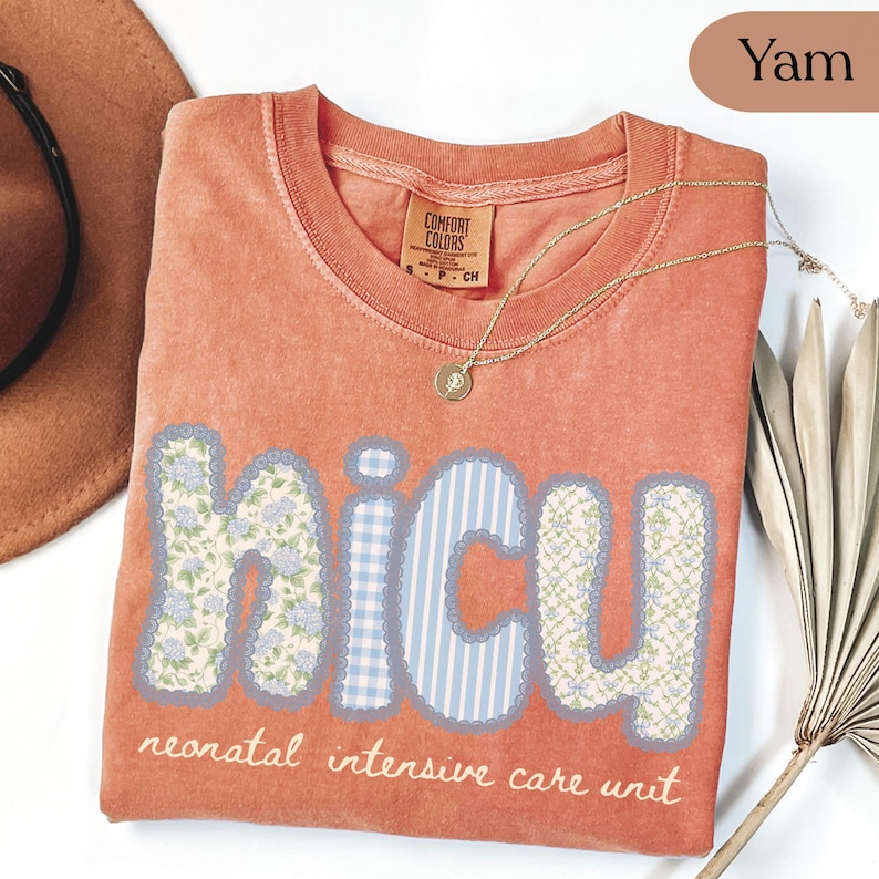 May include: A yam-colored Comfort Colors t-shirt with the word "NICU" in a patchwork design. The letters feature floral, gingham, and striped patterns. The text "neonatal intensive care unit" is below the letters. A gold necklace is draped across the shirt.