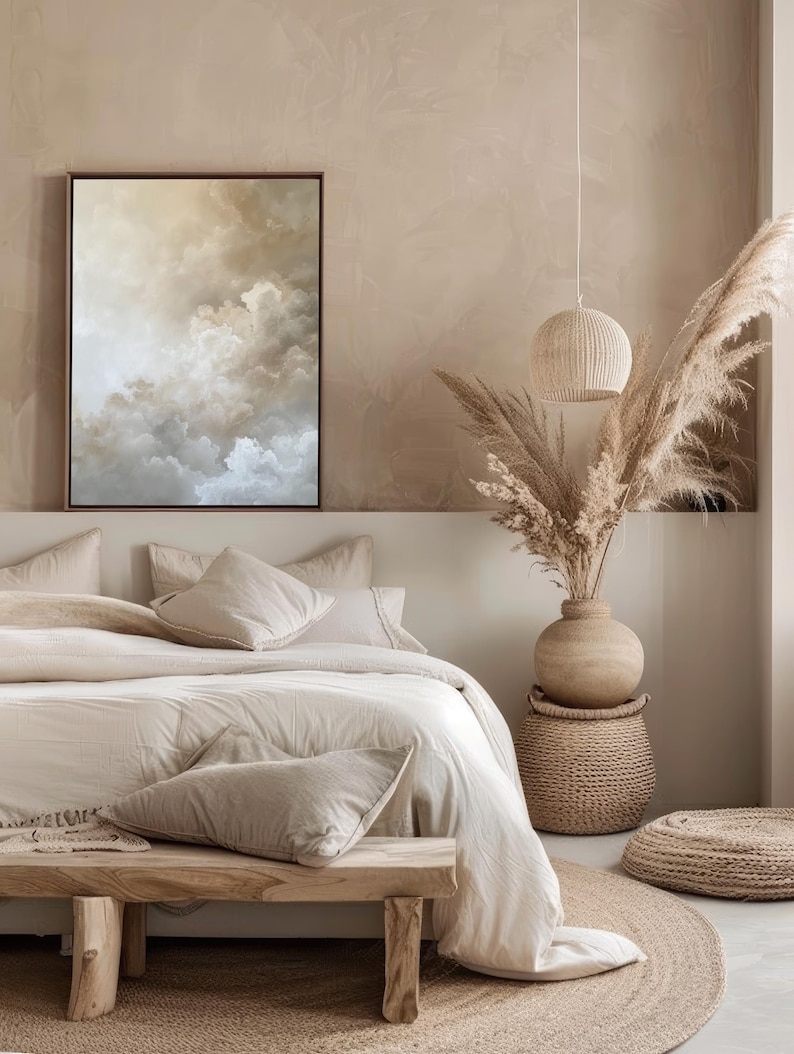 Peut inclure: Une chambre &agrave; coucher beige avec un lit, un banc en bois, une table d'appoint en osier, un vase avec de l'herbe de la pampa s&eacute;ch&eacute;e et un tapis rond en jute. Le lit est recouvert d'une couette blanche et de plusieurs oreillers beiges. Un tableau abstrait encadr&eacute; repr&eacute;sentant des nuages ​​est accroch&eacute; au mur au-dessus du lit.