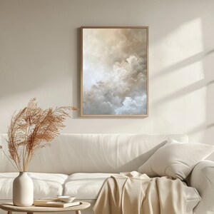Peut inclure: Une peinture abstraite encadr&eacute;e de nuages dans des tons beige, brun et blanc. La peinture est accroch&eacute;e &agrave; un mur blanc au-dessus d'un canap&eacute; blanc avec une couverture.