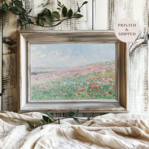 May include: A framed painting of a field of wildflowers in shades of pink, red, and white. The field is set against a blue sky with white clouds. The painting is in a rustic white frame.