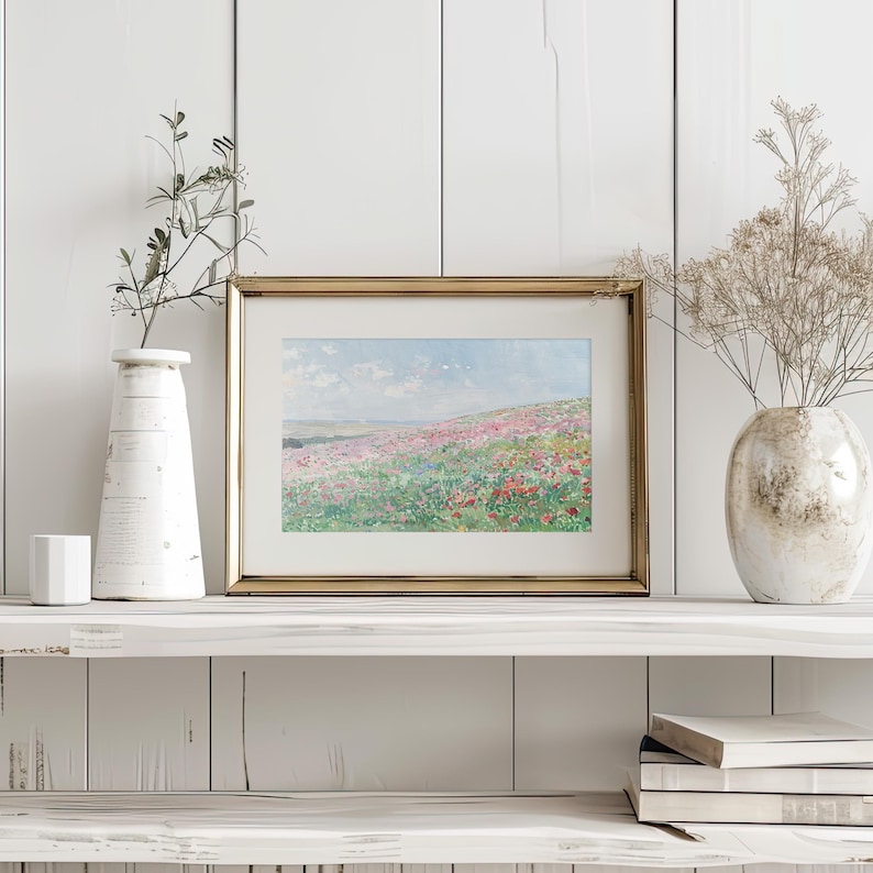 May include: A framed painting of a field of wildflowers in shades of pink, purple, and white. The painting is set against a backdrop of a blue sky with fluffy clouds. The frame is gold and has a simple design.