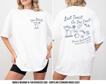 May include: Two white t-shirts with different designs. The front shirt says "The Bride" with a cocktail glass graphic. The back shirt says "Last Toast On The Coast" with a cocktail glass, seashells, and starfish graphic. The text "Olivia's Bachelorette Fort Lauderdale, Florida Est. 2025" is below the graphic.