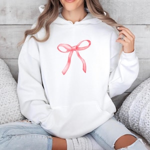 Könnte beinhalten: Weißer Hoodie mit einem rosafarbenen Aquarell-Schleifendesign auf der Vorderseite.