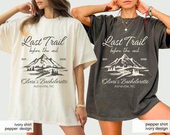 May include: Two t-shirts, one ivory and one pepper-colored, featuring the text "Last Trail before the veil" and "Olivia's Bachelorette Asheville, NC". The design includes a mountain range and river illustration.