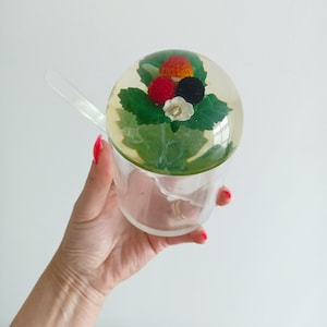 Peut inclure: Un distributeur de sucre en verre transparent avec un couvercle rond orné d'un motif de fleurs pressées. Le couvercle présente une fleur rouge, blanche et noire avec des feuilles vertes.