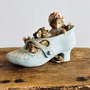 May include: A blue ceramic shoe with a white lace design and a group of mice inside. The mice are brown and gray and have small, delicate features. The shoe has a high heel and a pointed toe.