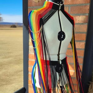 Könnte beinhalten: Ein regenbogenfarbenes gehäkeltes Oberteil mit schwarzen Trägern und einem schwarzen Choker. Das Oberteil hat lange Fransen und ein Kettendetail an der Schulter.