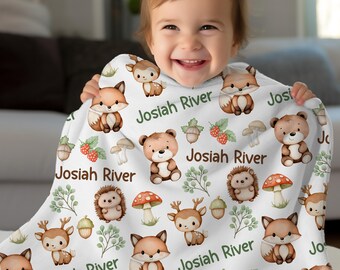 May include: A white baby blanket featuring a woodland animal pattern with foxes, bears, deer, hedgehogs, mushrooms, and berries. The name "Josiah River" is printed in green script across the blanket.