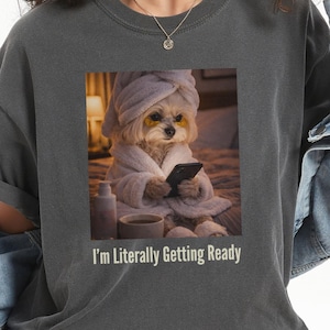 May include: Dark gray t-shirt featuring a graphic of a dog in a spa robe and towel, holding a phone. The text "I'm Literally Getting Ready" is below the image. The shirt is worn by a person.