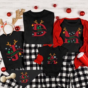 May include: A set of four black Christmas pajamas with red and green reindeer designs. The pajamas feature the names "Dad", "Mom", "Jordan", and "Ava" in a festive font. The pajamas are paired with black and white plaid pants.