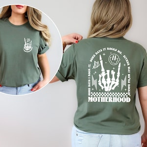May include: A green t-shirt with a white graphic on the back that says "Some days I rock it. Some days it rocks me. Either way we're rockin' Motherhood." The graphic includes a skeleton hand making a rock and roll sign, a butterfly, and a smiley face.