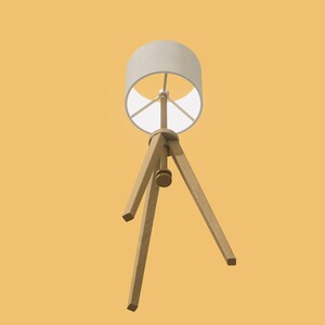 May include: A white lampshade with a wooden tripod base. The lampshade is cylindrical and has a white fabric covering. The tripod base is made of three wooden legs that meet at a point in the center of the lampshade.