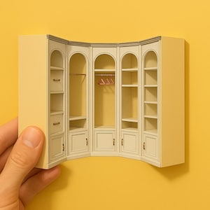 Könnte beinhalten: Ein weißer Eck-Schrank mit drei Abschnitten, jeder mit Regalen und einer Tür. Der Schrank hat eine gebogene Vorderseite und goldfarbene Beschläge. Im mittleren Abschnitt befinden sich zwei rosa Kleiderbügel.