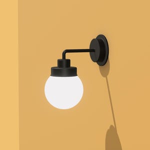 以下が含まれることがあります： 白い球形のシェードが付いた黒い壁掛け照明器具。照明器具は黄色の壁に取り付けられています。